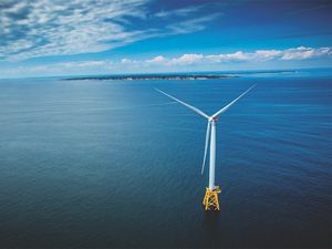 An aerial view of a wind turbine in the ocean, with the coast of Block Island and Rhode Island in the background.