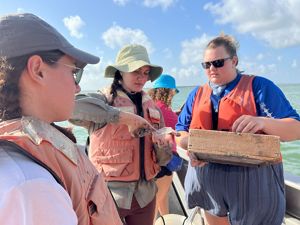 Four women stand on a boat examining a container with samples.