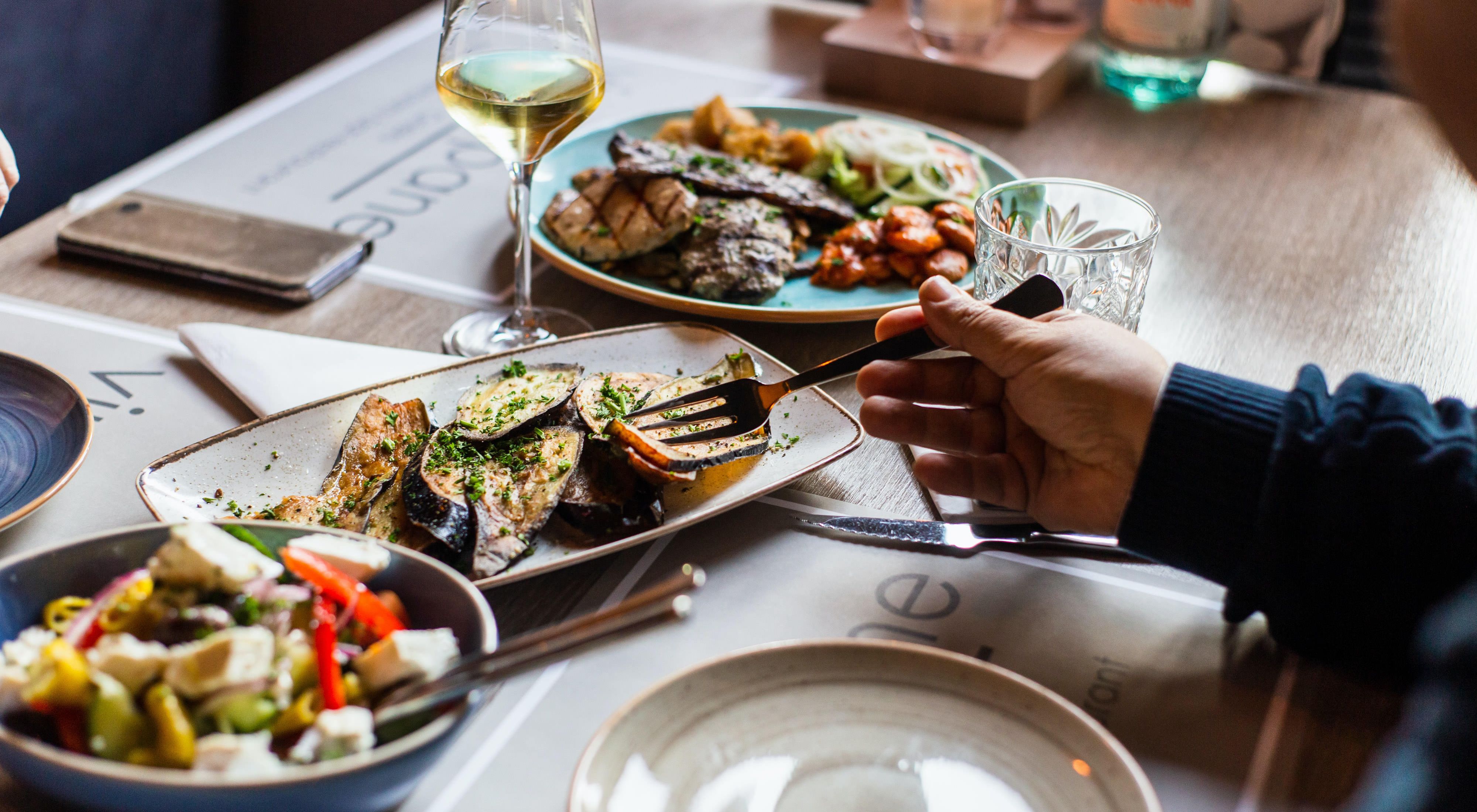 a person's arms pictured sitting at a dinner table with a variety of food on the table