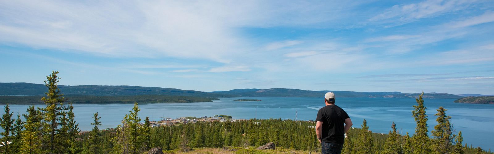 A man looks out at water and trees while standing on a high vantage point.