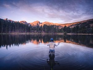 Photo of a man flyfishing in a pond in Rocky Mountain National Park, mountains in background.