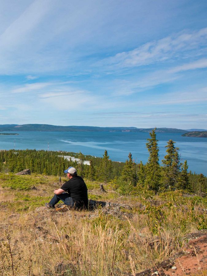 A person sits on a cliff overlooking water.