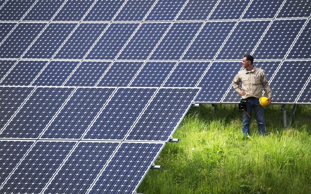 Photo of a man with hardhat standing beside newly installed solar array.