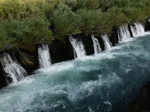 Blue river water cascades and froths over a natural wall of rock.