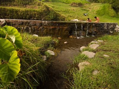 Two people sit on a brick wall from which water cascades into a stream.