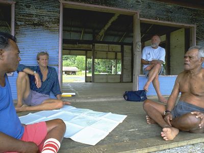 Group of men converse over an architectural plan in an office under construction.