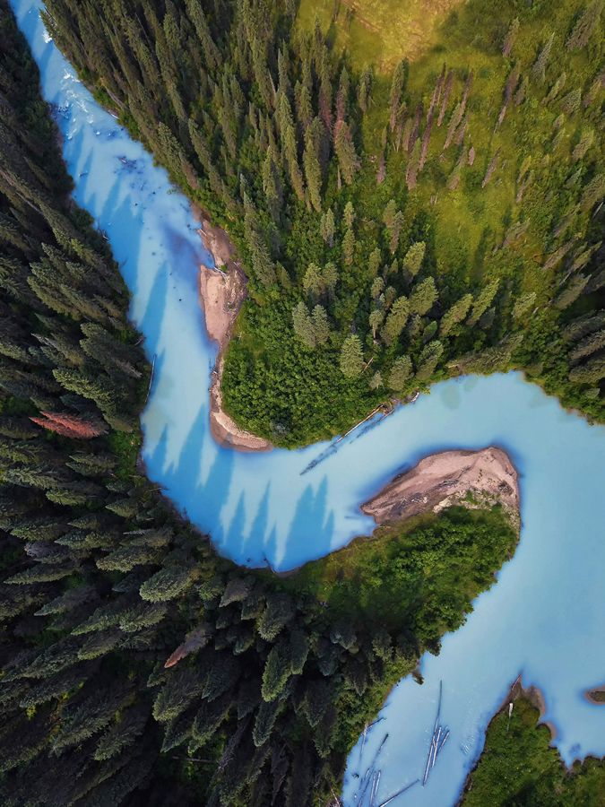 Aerial view of a sky-blue river running through forest.