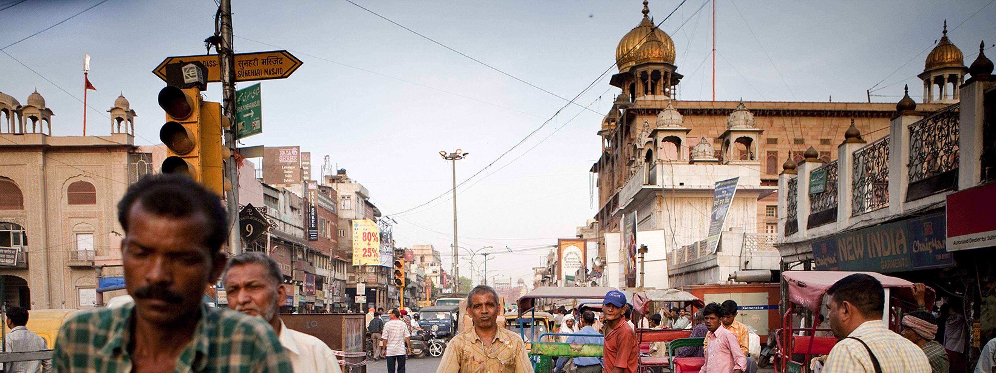 Dozens of people, rickshaws, and motor vehicles crowd a street in New Delhi, India.