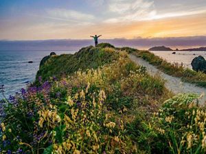 A woman with arms outstretched on a hill overlooking the ocean 