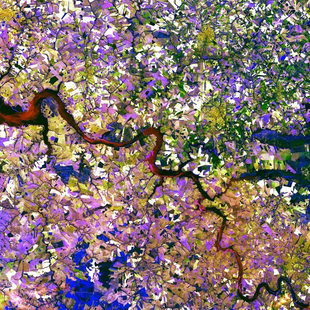 Aerial view looking straight down on a winding river snaking through a multicolored landscape.