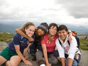 Four people sit together at a mountain overlook. There arms are linked around each others necks as they lean in and post together.