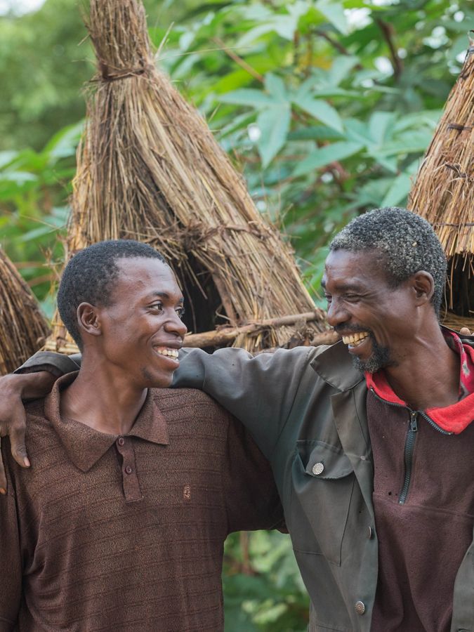 Two smiling men arm-in-arms, in a small village.